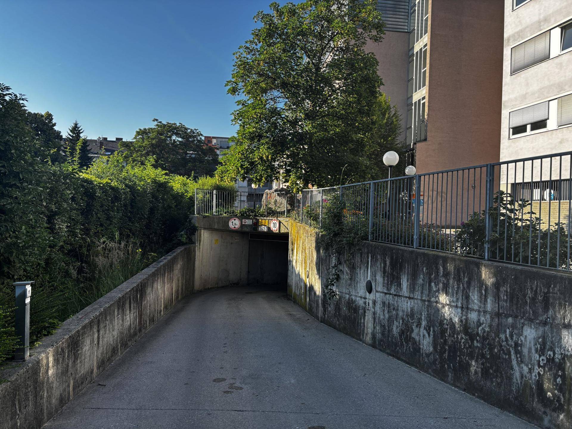 Außenansicht der Tiefgarageneinfahrt, umgeben von üppigem Grün und einem modernen Wohngebäude.