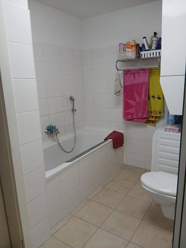 Helles Badezimmer mit weißen Fliesen, Badewanne und wandhängendem WC.