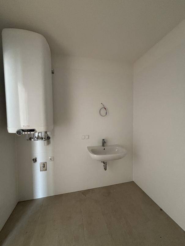 Kleiner Raum mit Warmwasserboiler und Waschbecken, ideal als Hauswirtschaftsraum nutzbar.