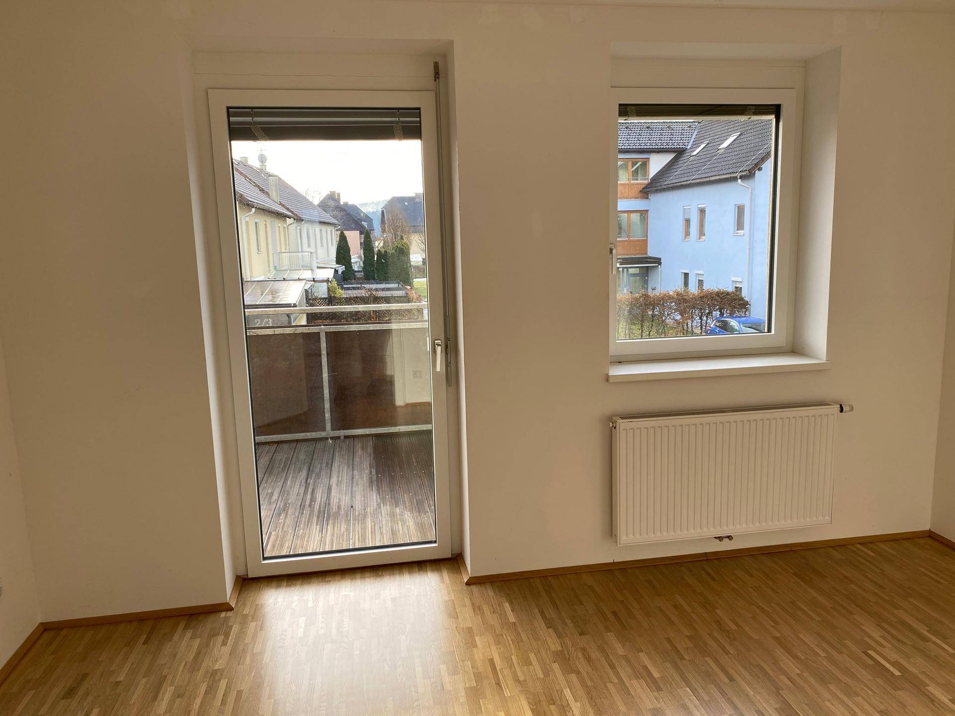 Heller Wohnraum mit Holzboden, Heizkörper und Zugang zu einem Balkon.