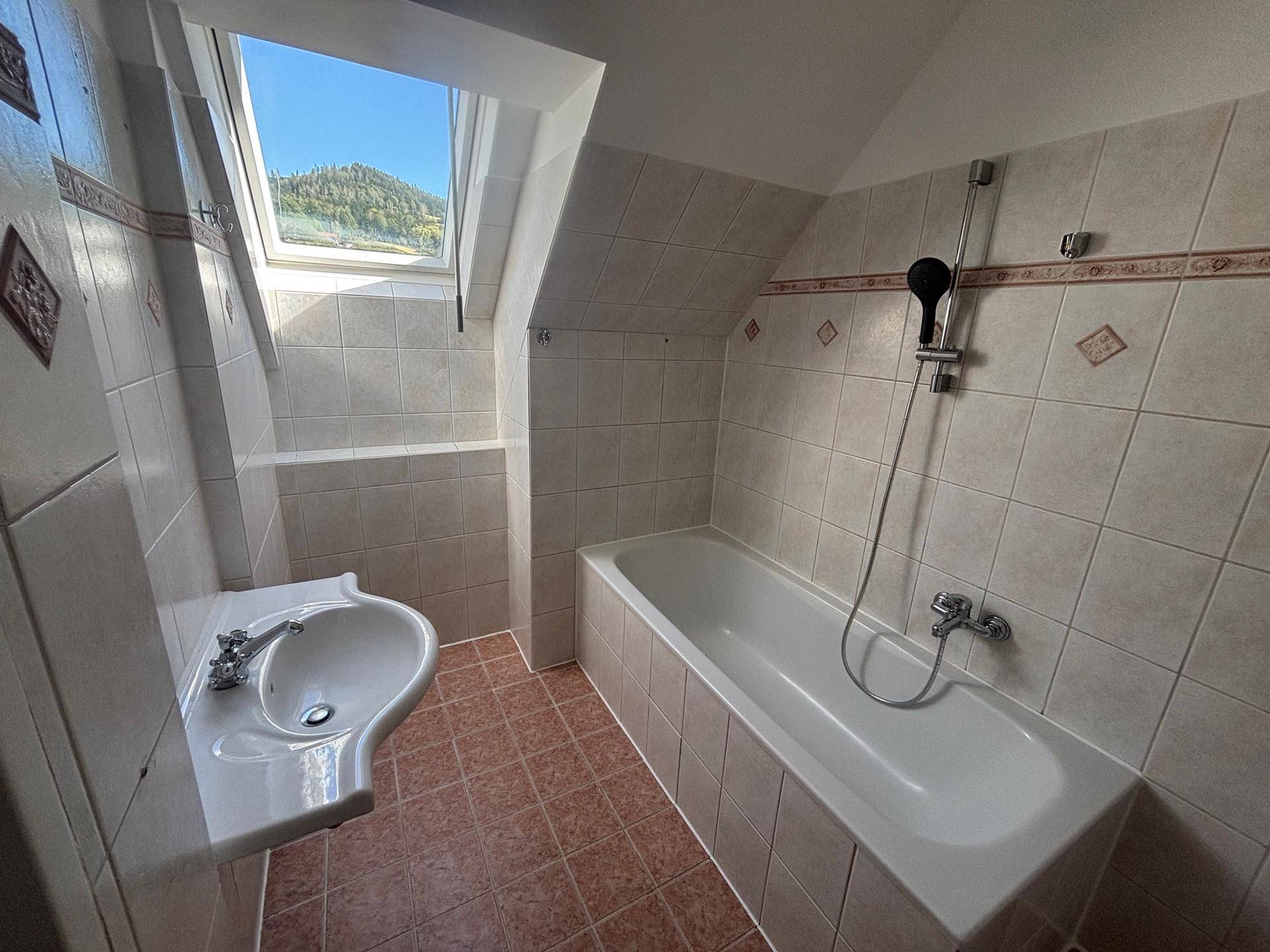 Badezimmer mit Badewanne, Waschbecken, beigefarbenen Fliesen und einem Dachfenster.