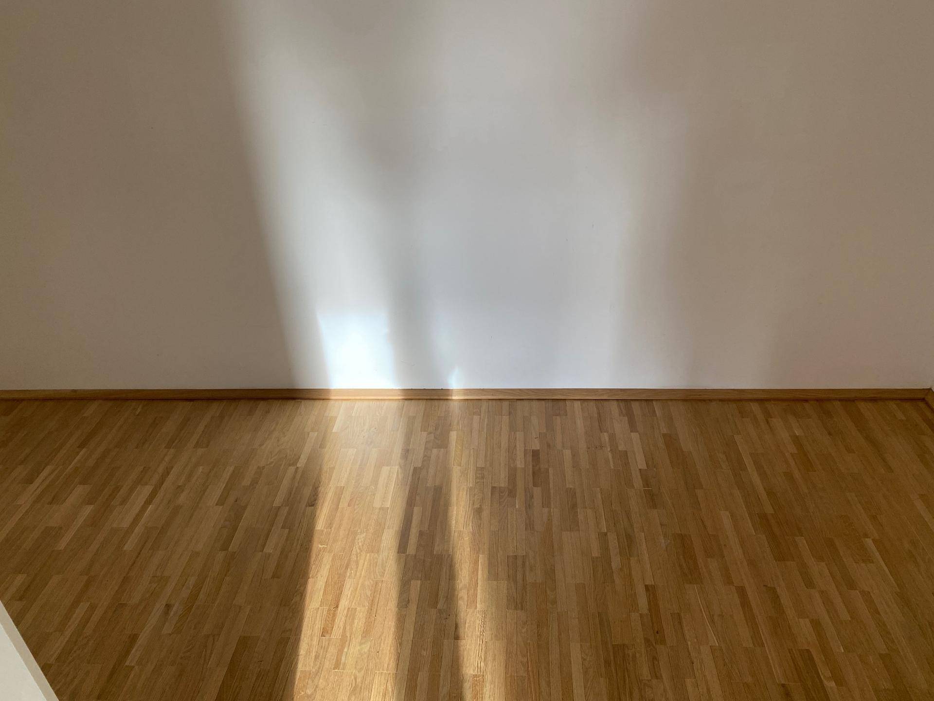 Heller Raum mit Holzboden und Sonnenlicht, das durch ein Fenster fällt.
