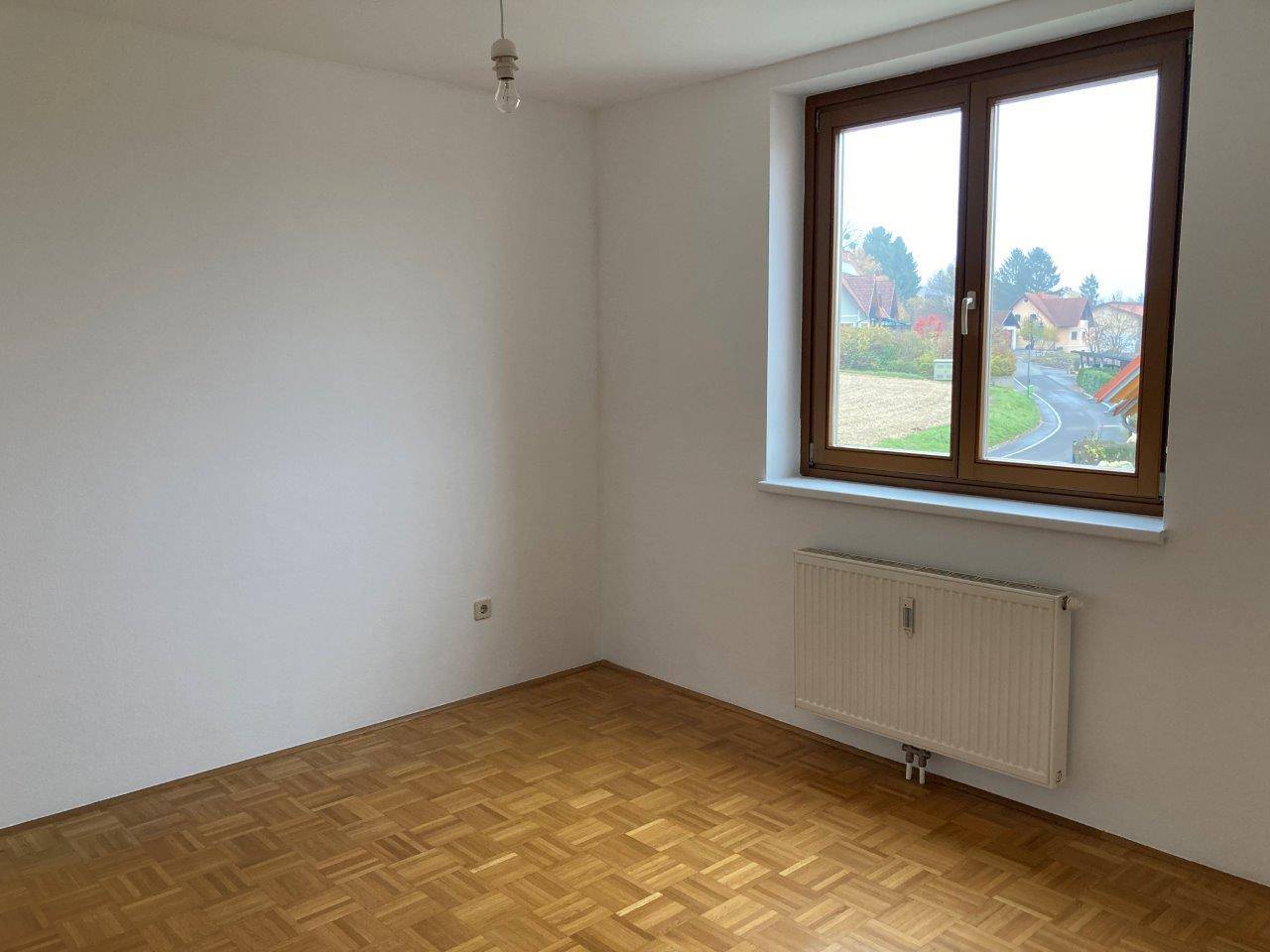 Leeres Zimmer mit Parkettboden, weiß gestrichenen Wänden und Blick ins Grüne.