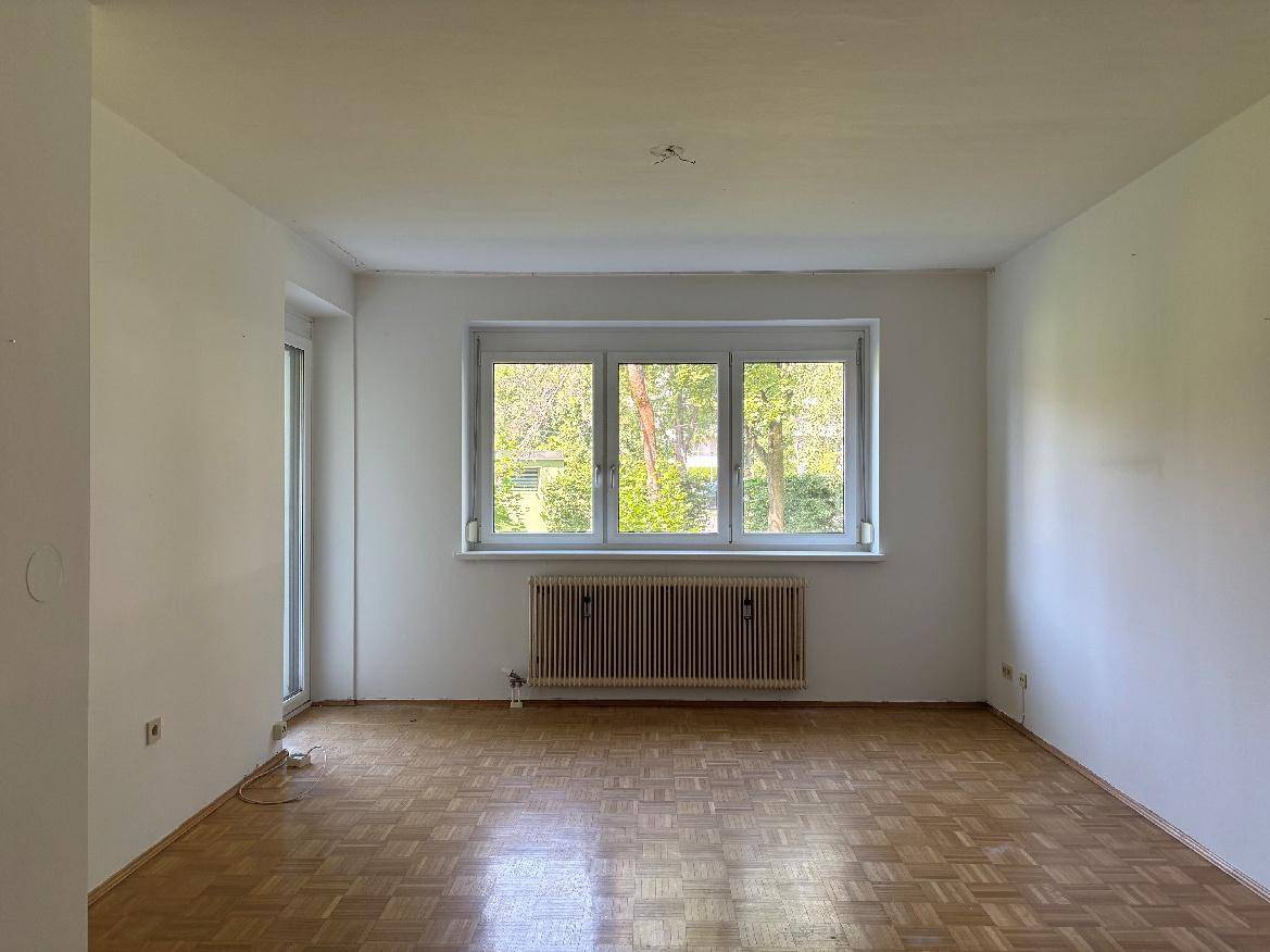 Helles Wohnzimmer mit Fischgrätparkettboden und großem Fenster mit Blick ins Grüne.