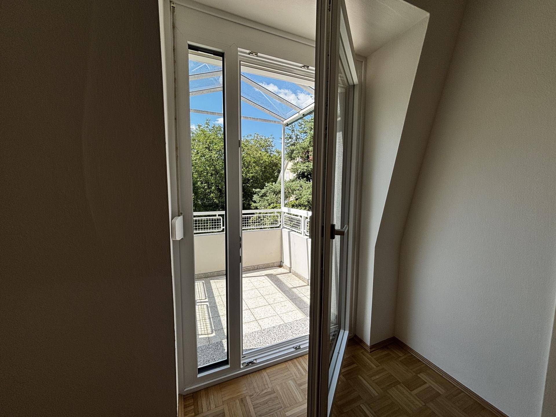 Zugang zu einem überdachten Balkon mit Fliesenboden und weitem Blick ins Grüne.