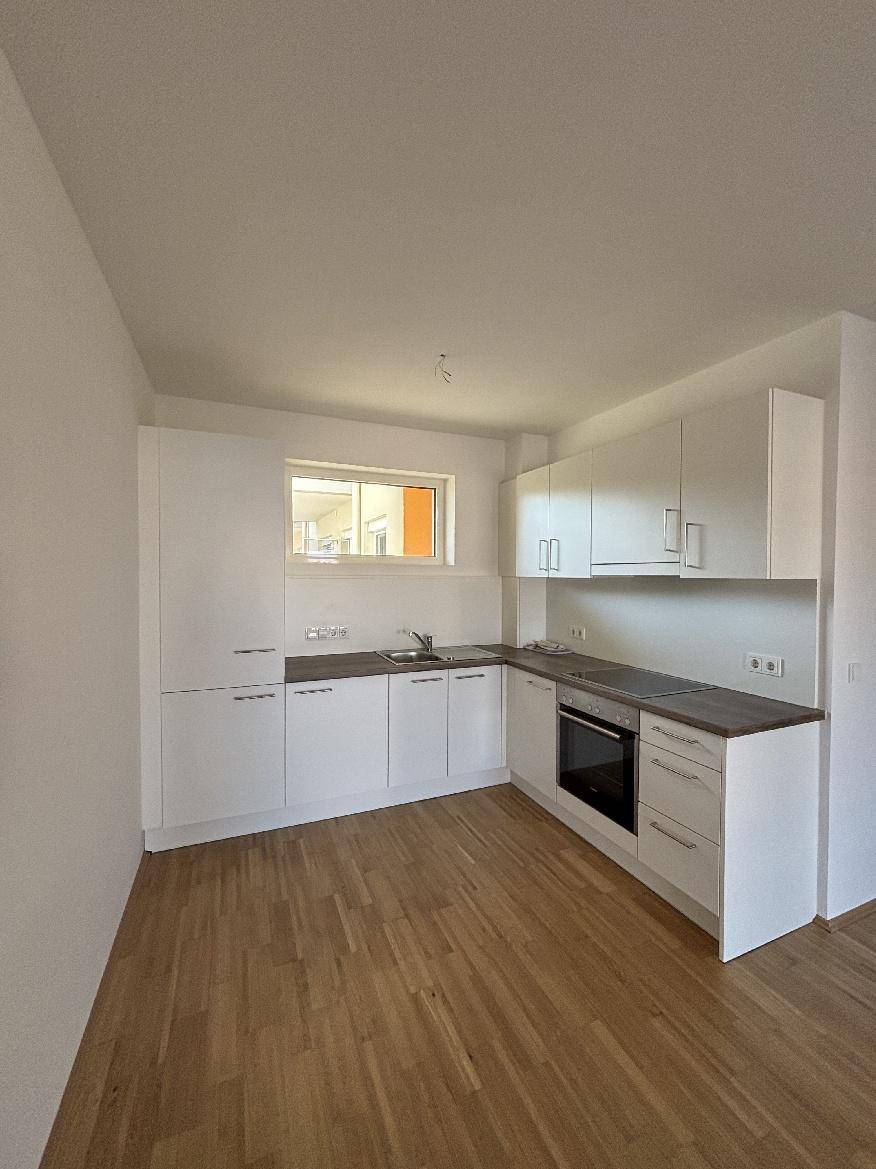 Moderne Einbauküche mit weißen Schränken, dunkler Arbeitsplatte und Holzparkettboden.