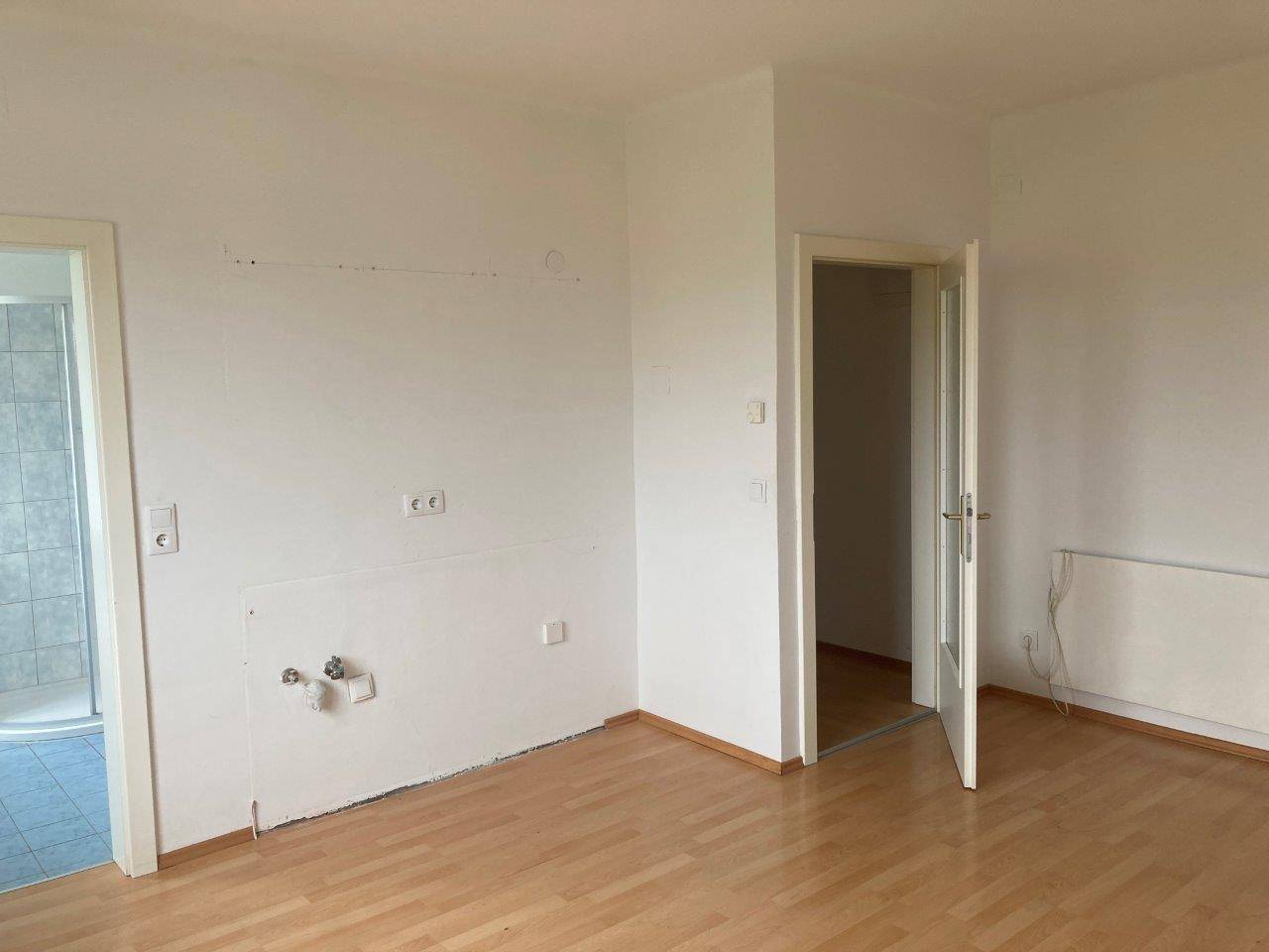 Leerer Raum mit Laminatboden und Zugang zu einem Badezimmer mit Duschkabine.
