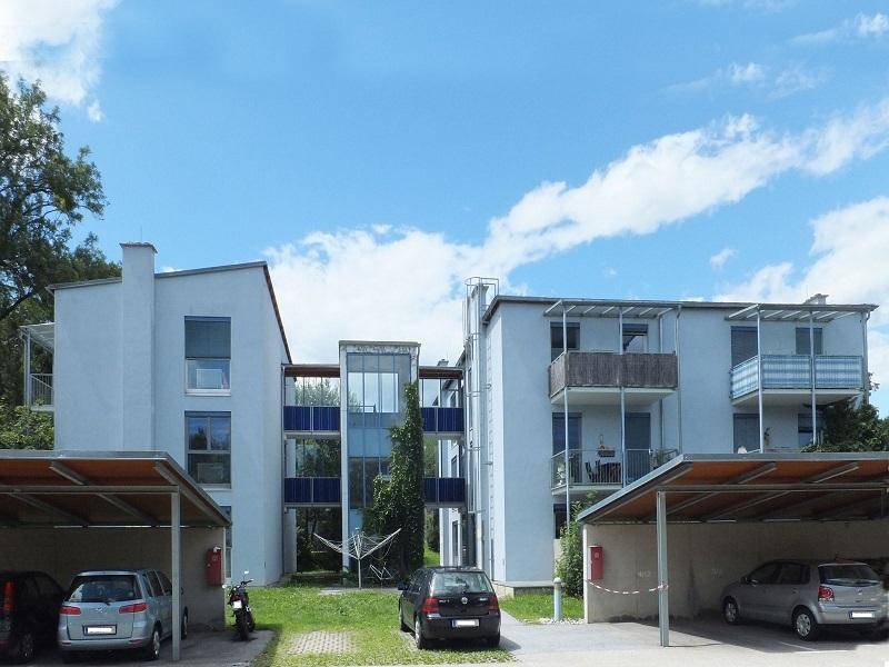 Mehrfamilienhaus mit Balkonen und überdachten Stellplätzen im Vordergrund.