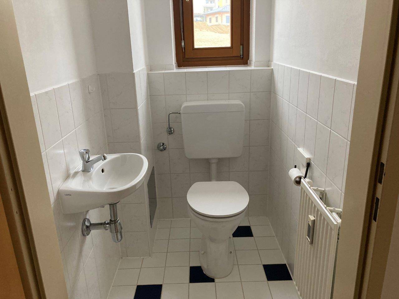 Kleines Gäste-WC mit Fenster, weißen Fliesen, Toilette und Einzelwaschbecken.