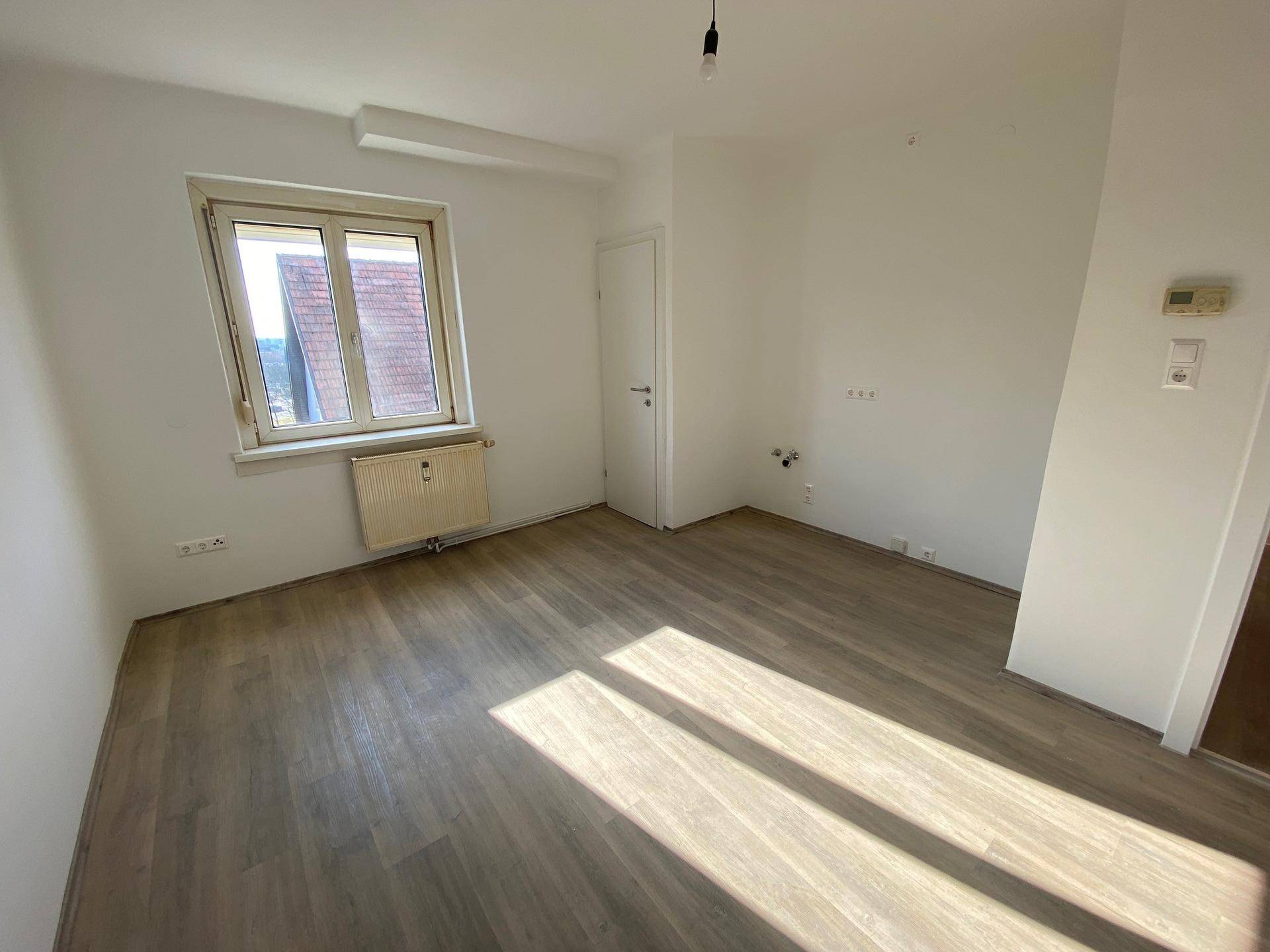 Heller Raum mit Laminatboden, großem Fenster und viel Tageslicht.