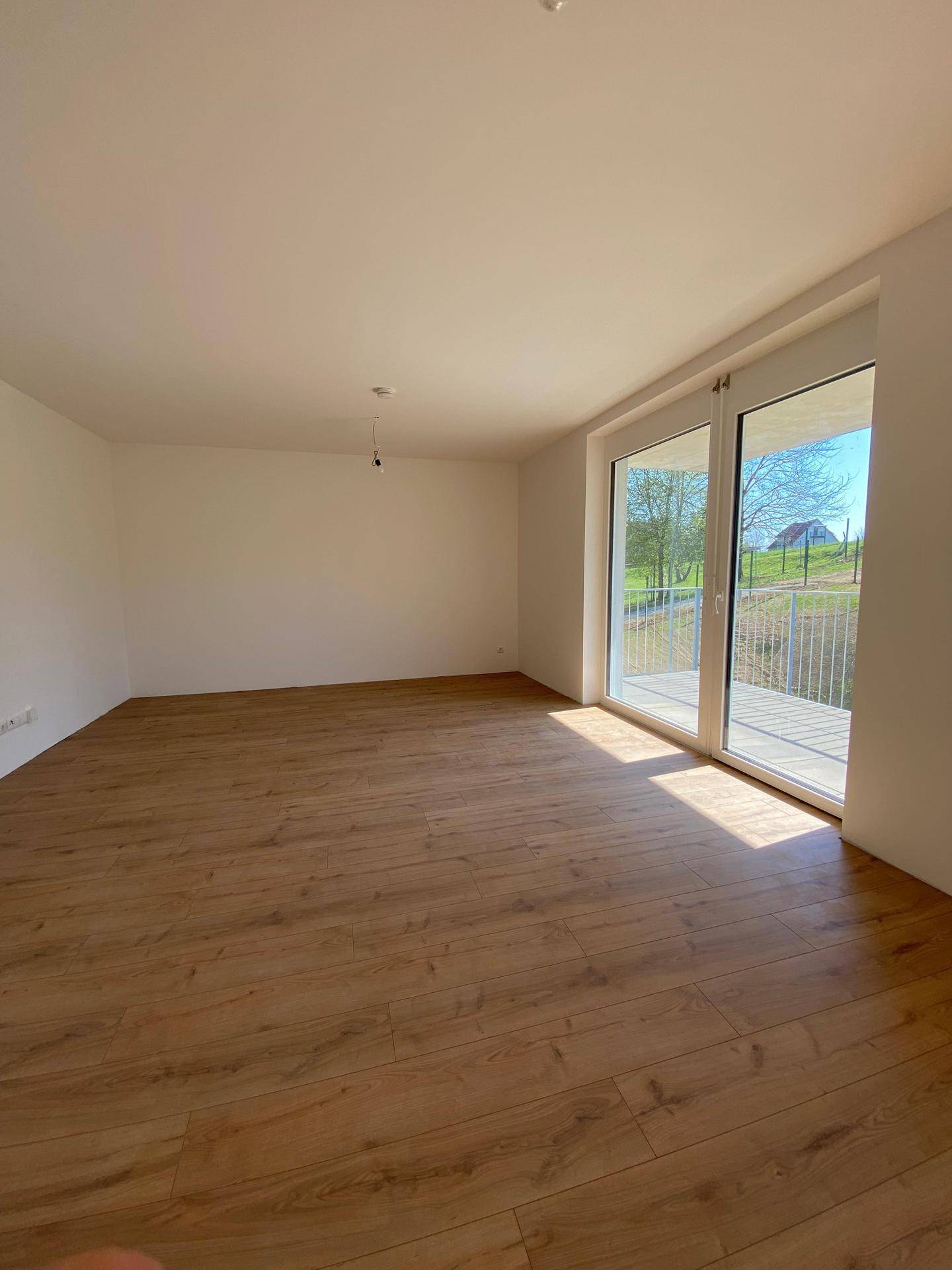 Helles Wohnzimmer mit Laminatboden und großen Fenstern, die Zugang zu einem Balkon bieten.