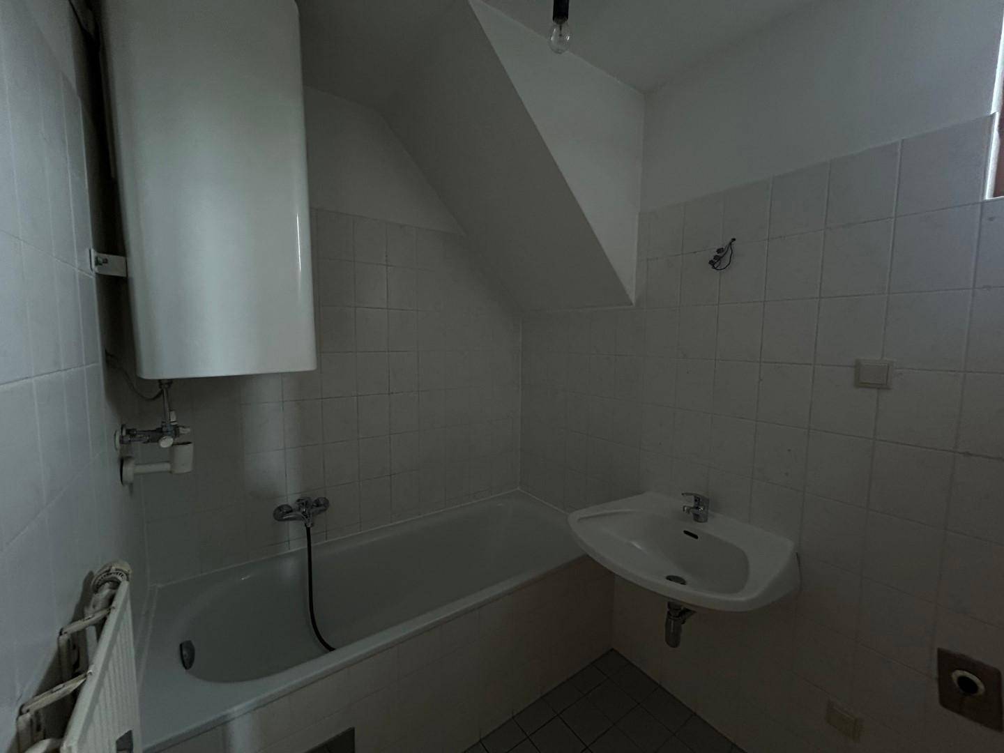 Badezimmer mit Badewanne, Waschbecken, Warmwasserboiler und Dachschräge.