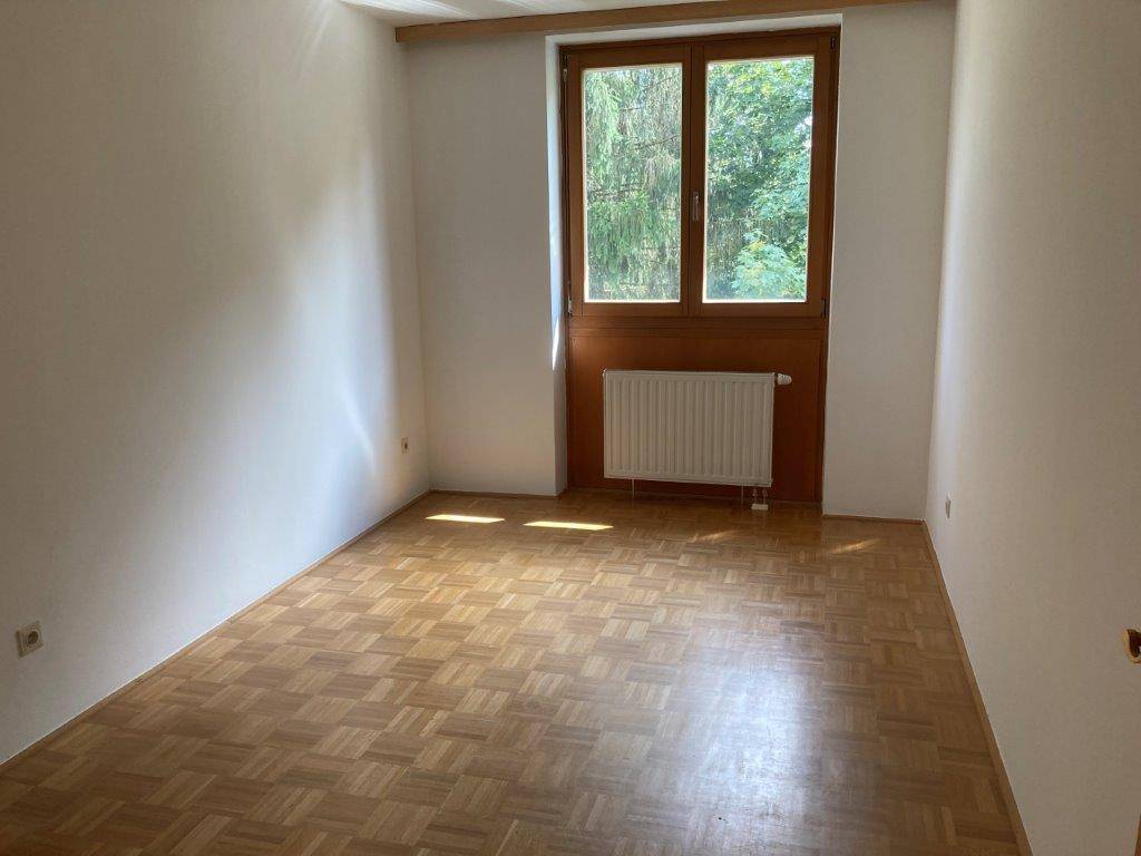 Schlafzimmer mit Parkettboden und großem Fenster, das den Blick ins Grüne freigibt.