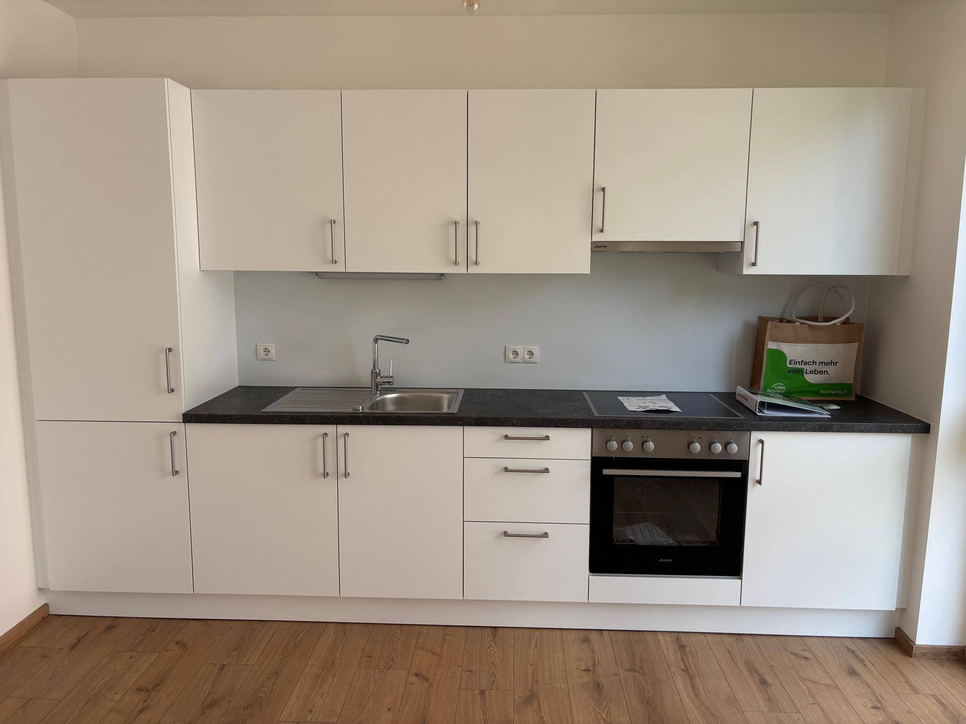 Neue, moderne Einbauküche in Weiß mit dunkler Arbeitsplatte und integrierten Geräten.