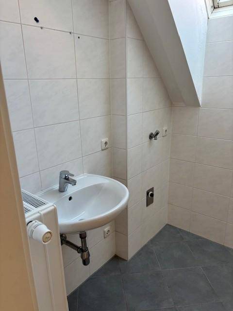 Kleines Badezimmer mit Waschbecken, Heizkörper und Dachfenster unter schräger Decke.