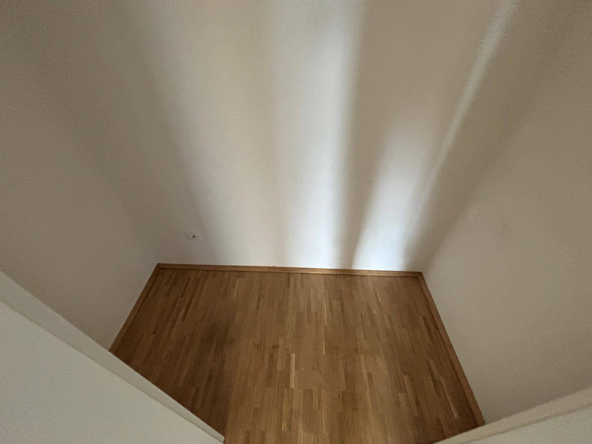 Innenraum mit Holzboden und schrägen Lichtstrahlen an der Decke, die eine besondere Atmosphäre schaffen.