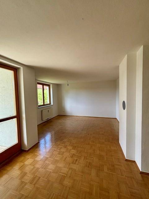 Geräumiges Wohnzimmer mit Parkettboden und Zugang zu einem Balkon oder einer Terrasse.