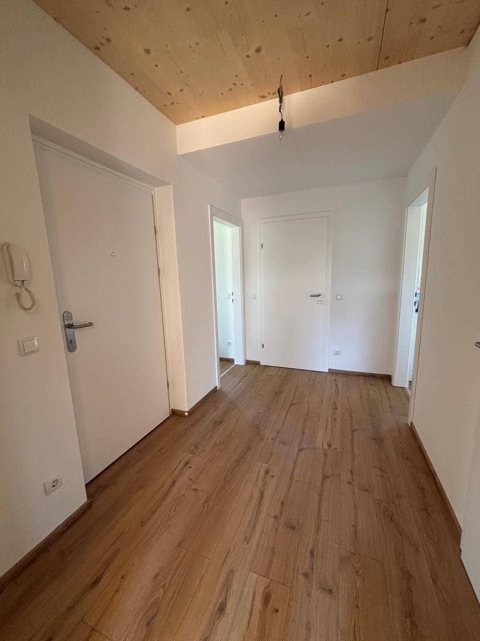 Heller Flur mit Holzboden und Holzdecke, mehreren Türen und einer Gegensprechanlage.