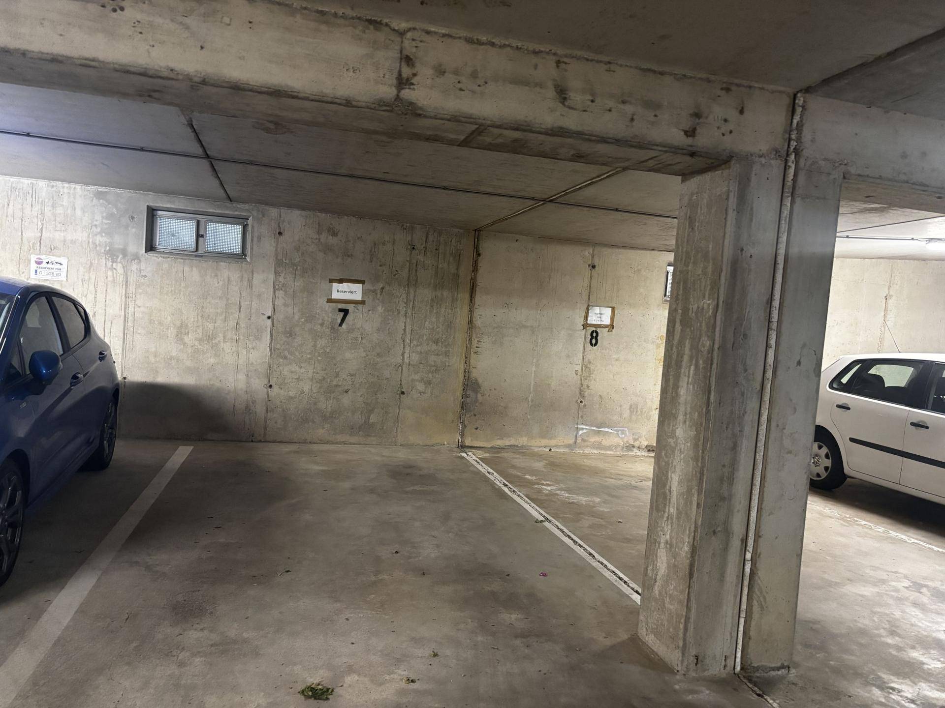 Betonierte Tiefgarage mit nummerierten Stellplätzen und geparkten Fahrzeugen in einer hellen Umgebung.