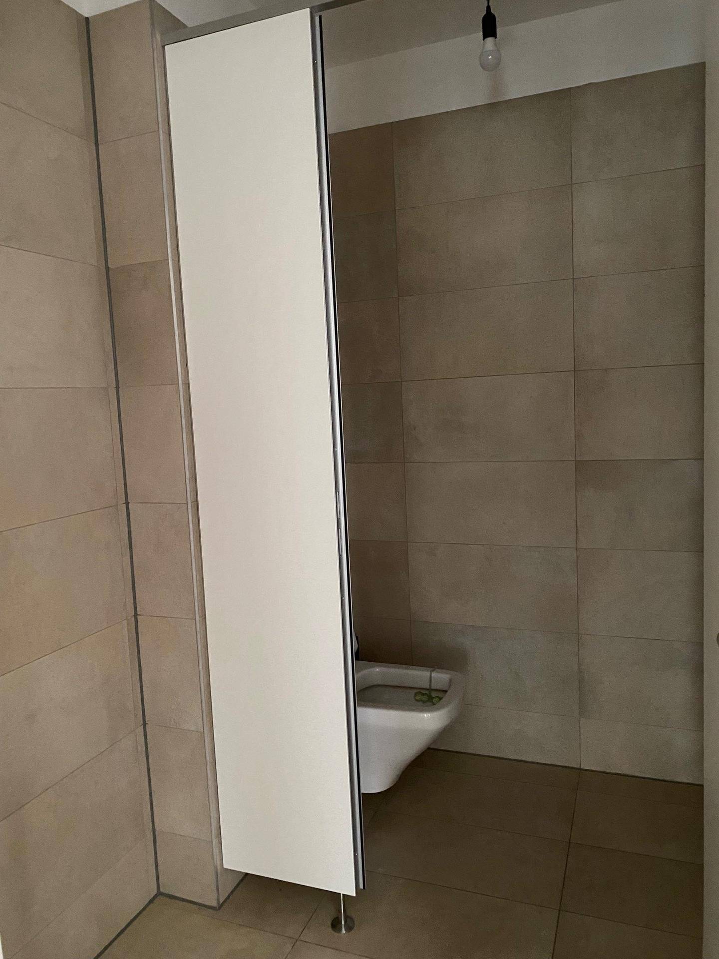 Separates WC mit wandhängender Toilette und beigefarbenen Wand- und Bodenfliesen.