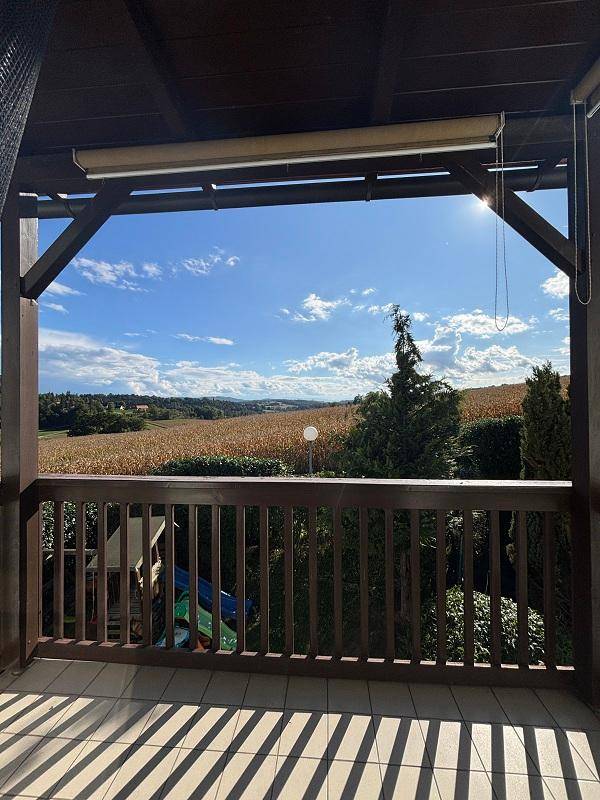 Überdachter Balkon mit Holzbalken und weitem Blick über Felder und die umliegende Landschaft.