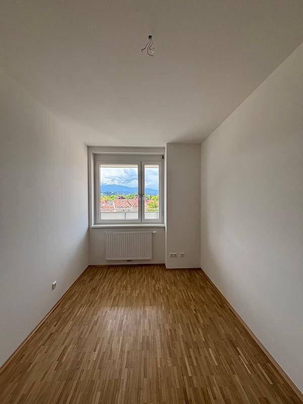 Helles Schlafzimmer mit Parkettboden, Fenster und Heizkörper, bietet einen weiten Ausblick.