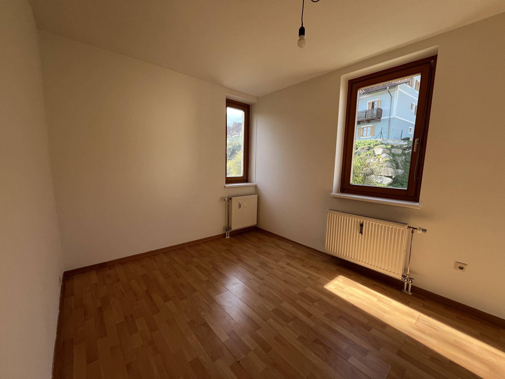 Helles Schlafzimmer mit Parkettboden und zwei Fenstern, die viel Licht spenden.