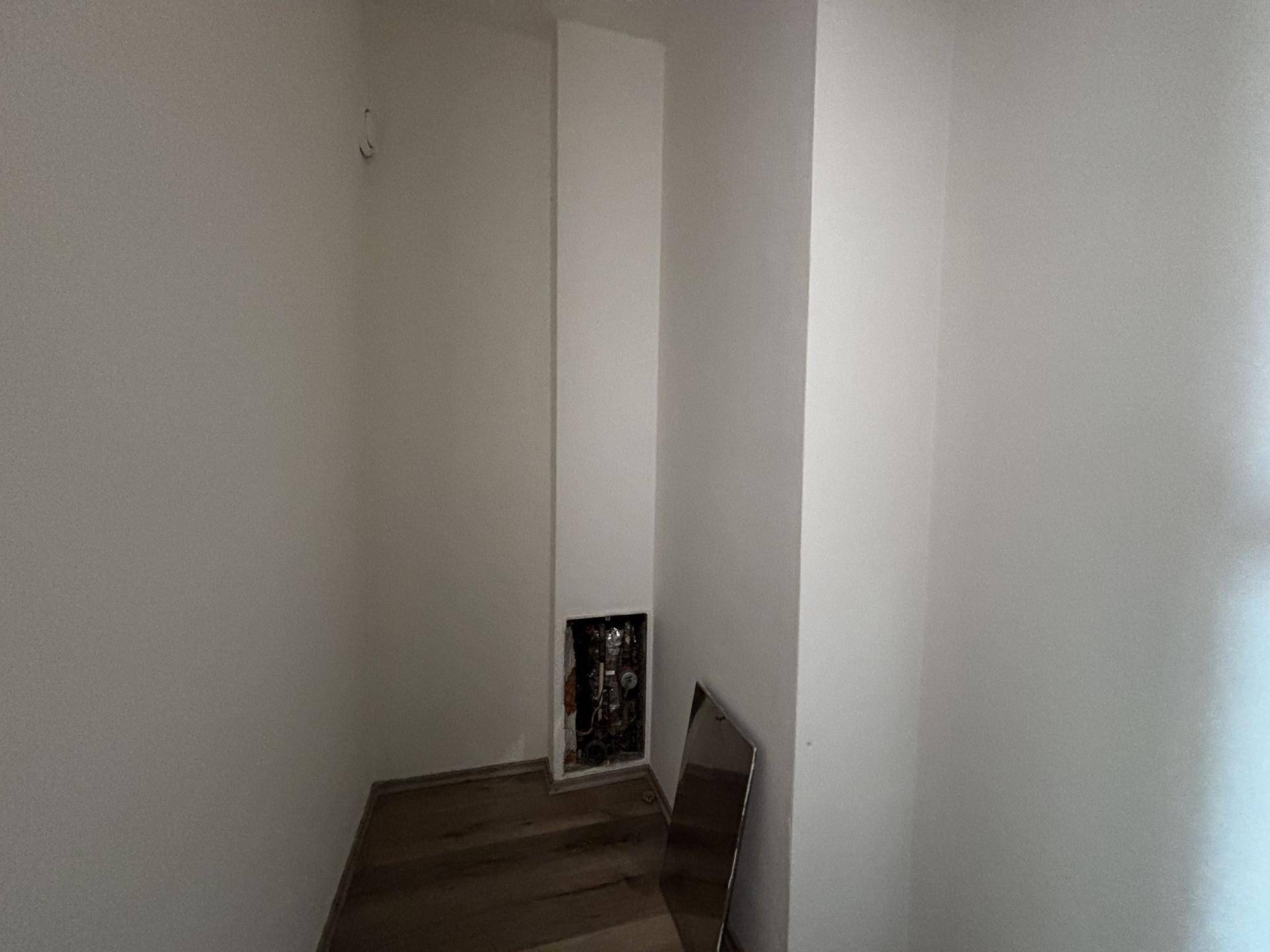 Kleiner leerer Raum mit Holzboden und einem offenen Sicherungskasten, ideal als Abstellraum.