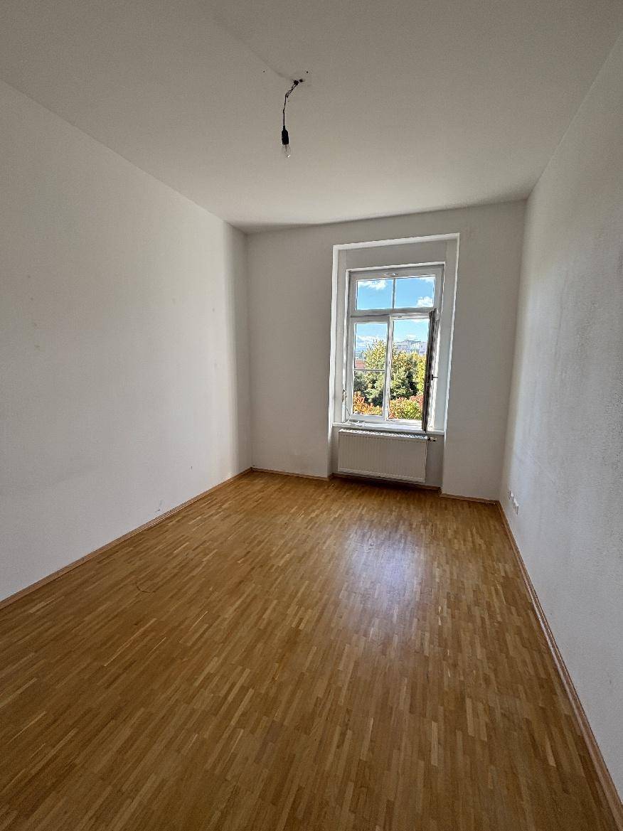 Geräumiges Zimmer mit Parkettboden, weiß gestrichenen Wänden und einem Fenster mit Ausblick.