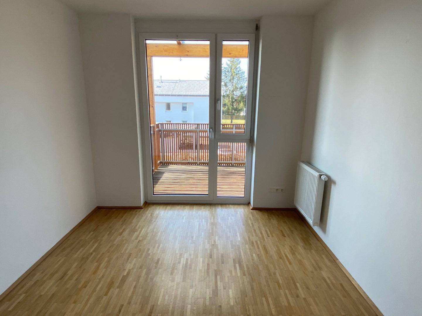 Schlafzimmer mit hellem Parkettboden und direktem Zugang zu einem sonnigen Balkon.