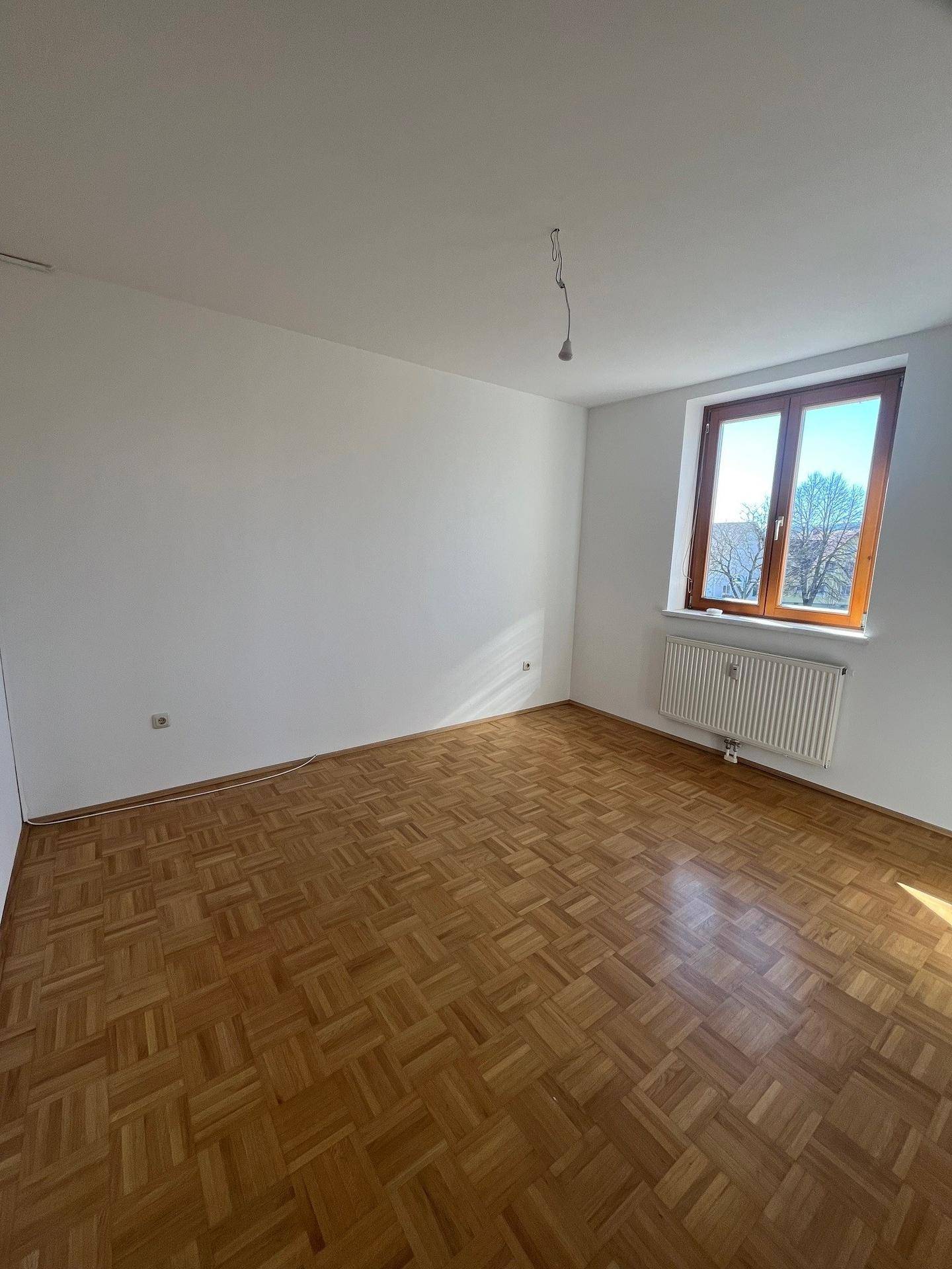 Freundliches Schlafzimmer mit Parkettboden, großem Fenster und viel Tageslicht, bietet eine angenehme Atmosphäre.