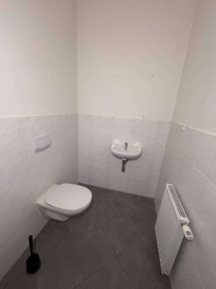 Separates WC mit wandhängender Toilette, kleinem Waschbecken und Fliesenboden.
