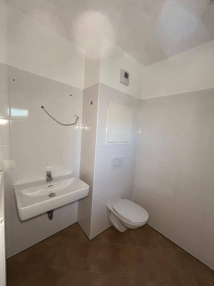 Modernes Gäste-WC mit wandhängendem Waschbecken und Toilette, hell gefliest und funktional.