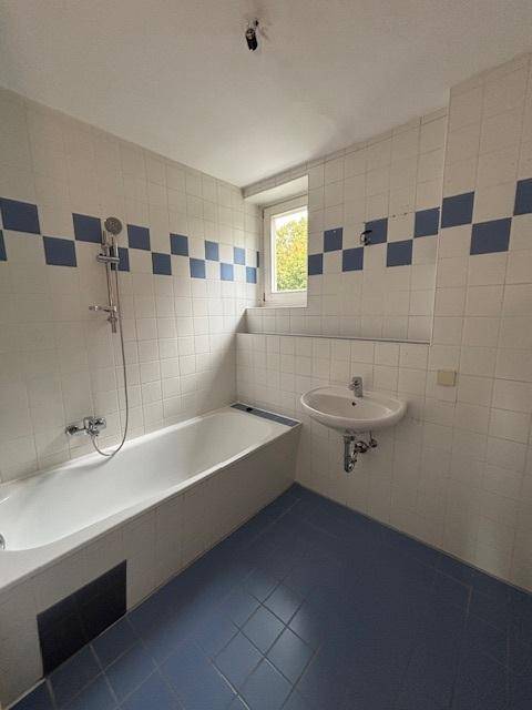 Badezimmer mit Badewanne, Waschbecken und Fenster, gefliest in Blau und Weiß.