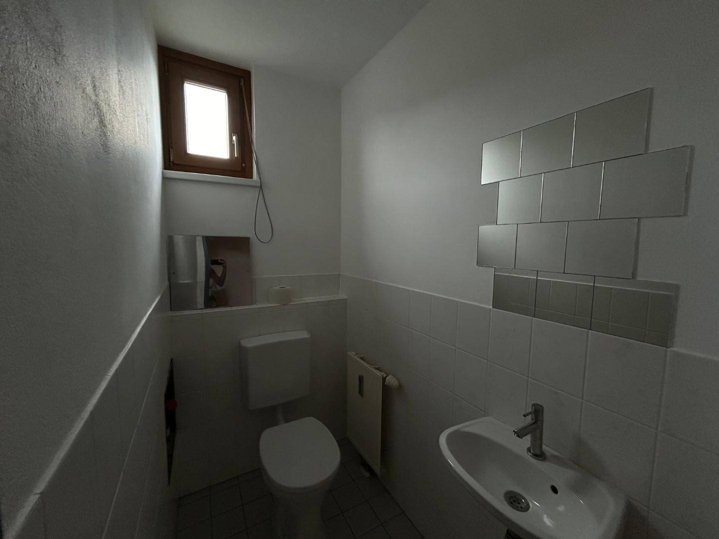 Kleines Gäste-WC mit Fenster, Waschbecken und weißen Fliesen.