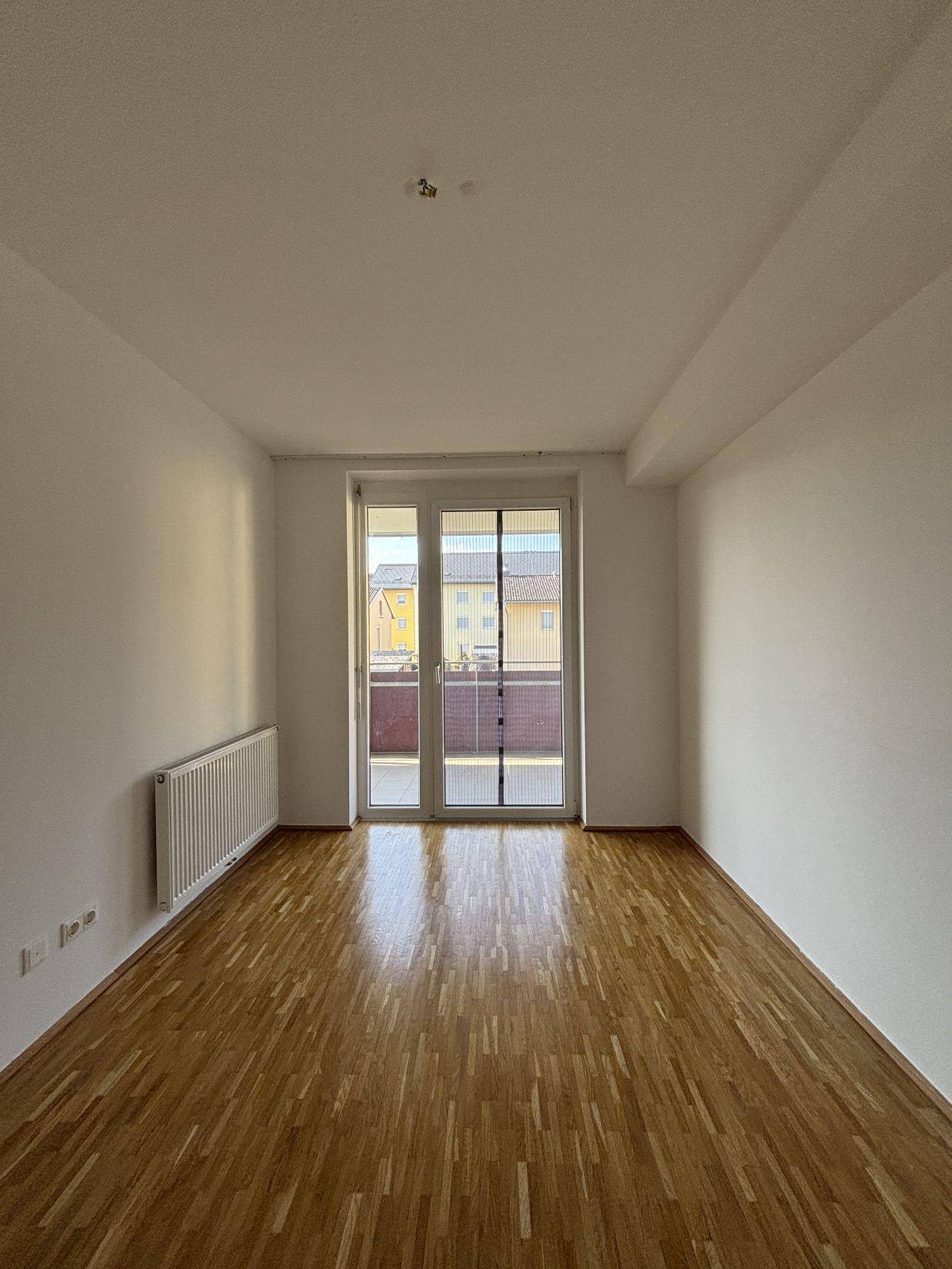 Heller Raum mit Parkettboden und breiter Balkontür, die viel Tageslicht hereinlässt.
