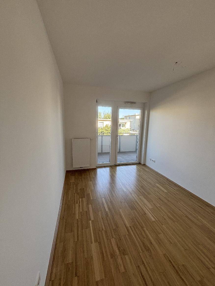 Helles Schlafzimmer mit Holzparkettboden und Zugang zu einem sonnigen Balkon.