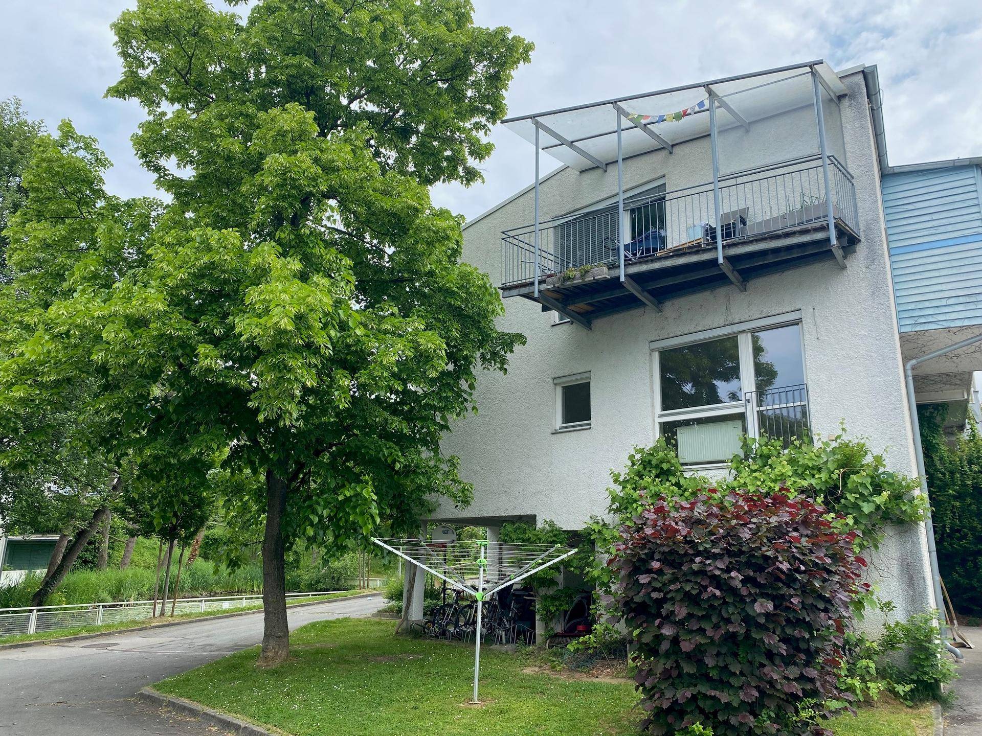 Balkon mit transparentem Dach, Wäscheleine und umgeben von Bäumen und Grünflächen.