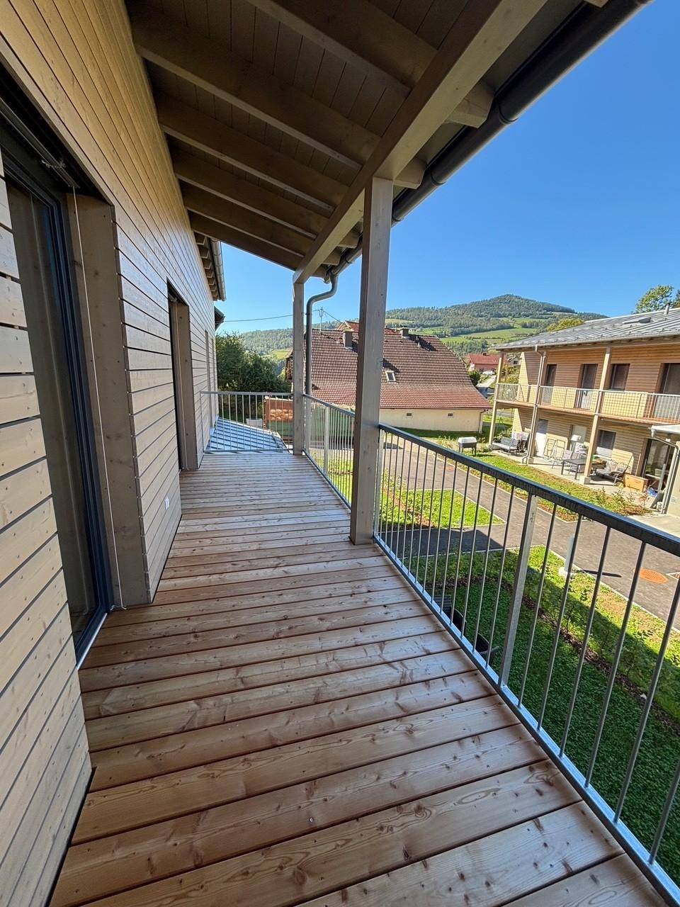 Langer Holzbalkon mit Metallgeländer und weitem Blick auf die umliegende Landschaft und Berge.