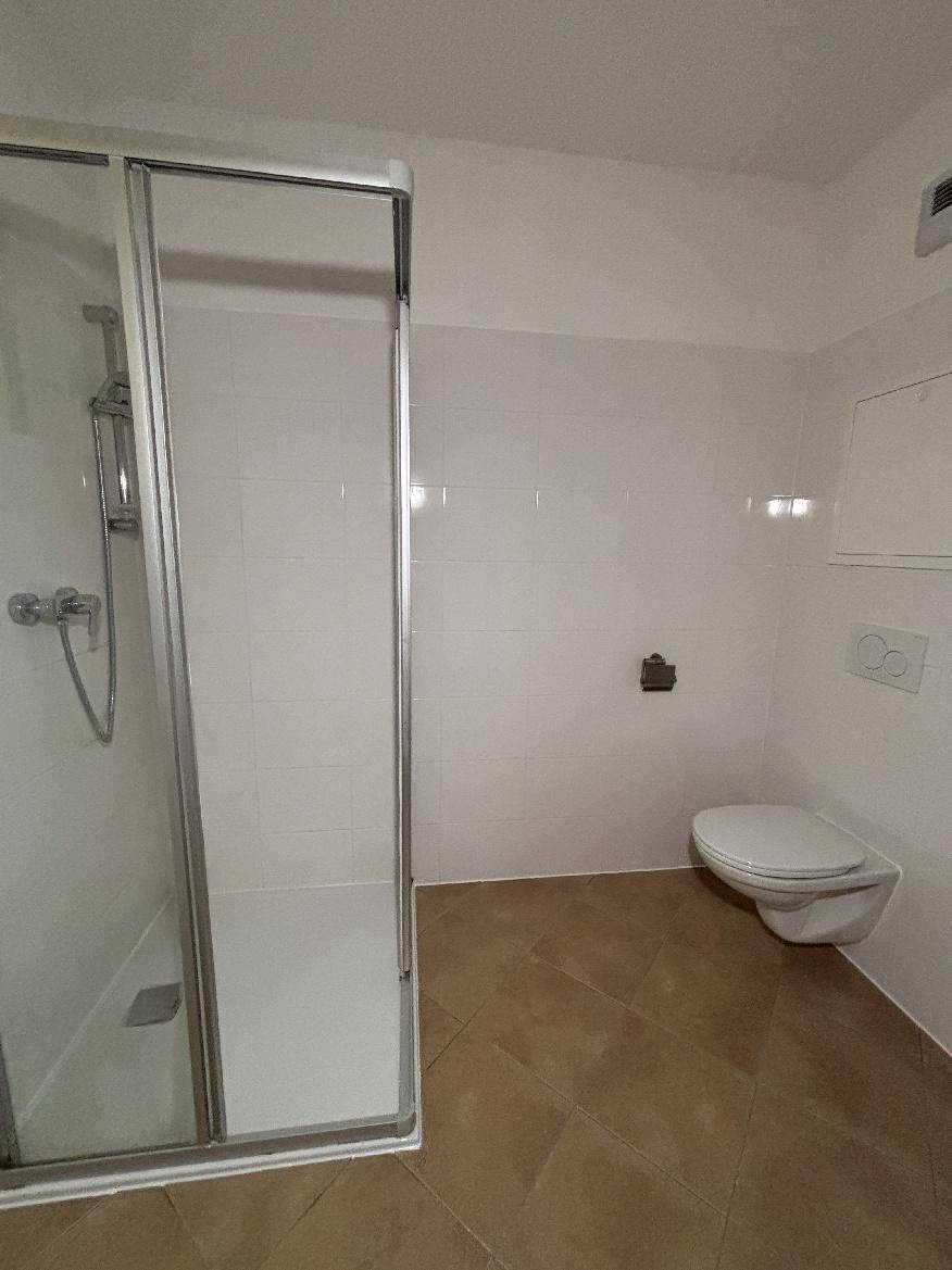 Modernes Badezimmer mit Duschkabine, wandhängendem WC und hellen Fliesen.