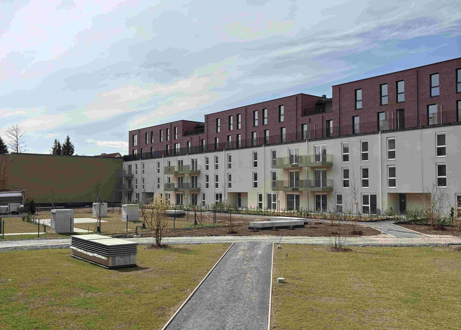 Neubau-Wohngebäude mit moderner Fassade und angelegten Grünflächen im Außenbereich unter hellem Himmel.