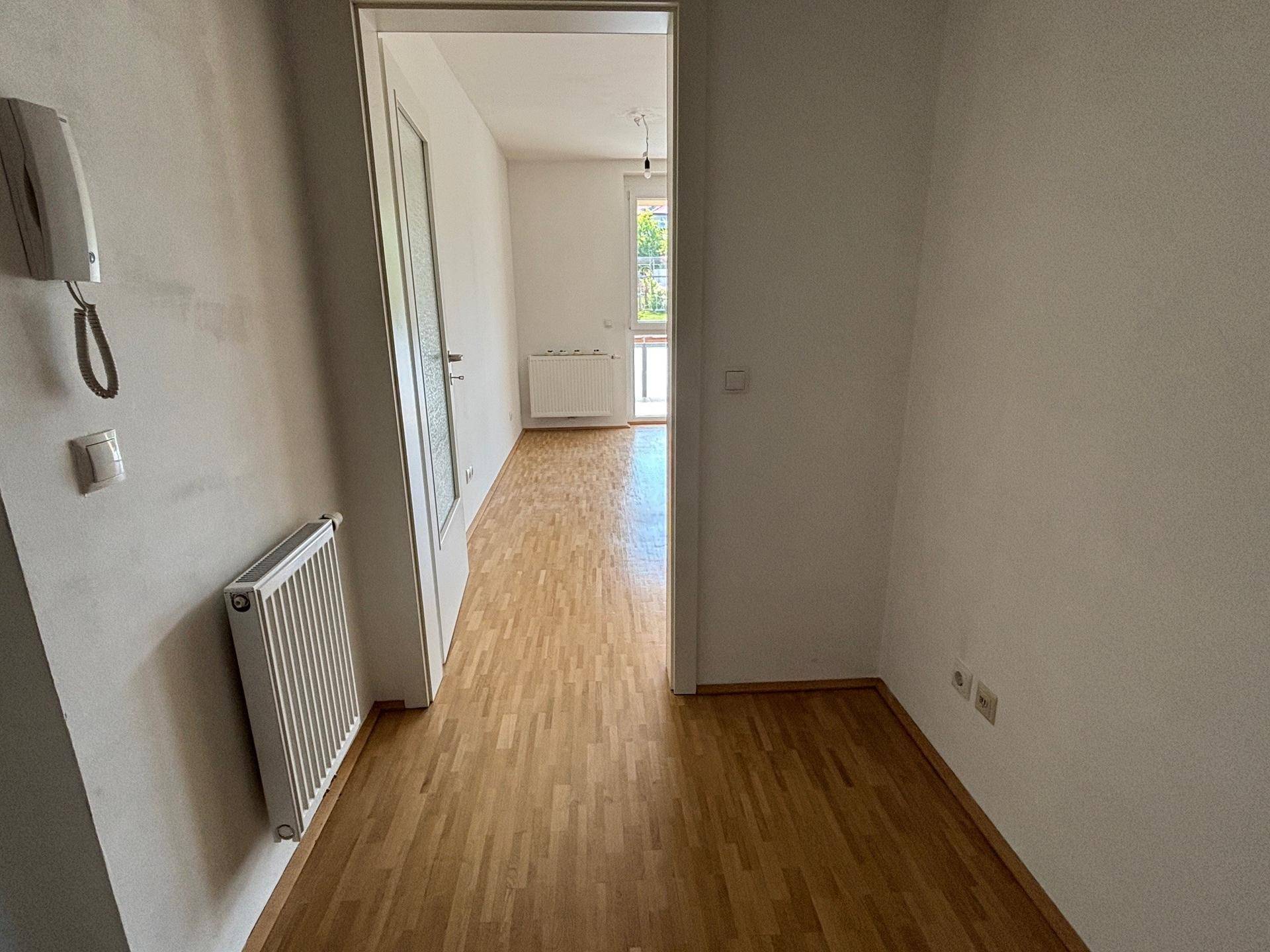 Heller Flur mit Holzboden und Gegensprechanlage, der zu weiteren Räumen führt.
