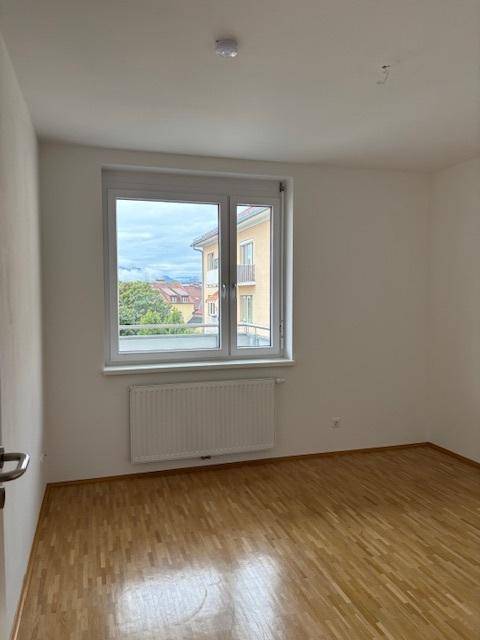 Helles Zimmer mit Parkettboden und Fenster, das viel Tageslicht in den Raum lässt.