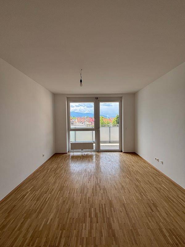 Heller Wohnraum mit Parkettboden, Balkonzugang und Bergblick in der Ferne.