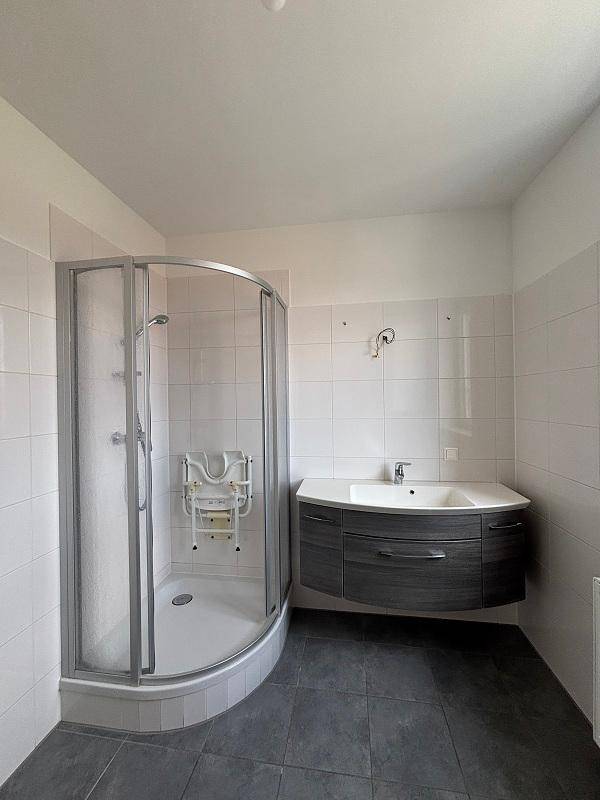 Modernes Badezimmer mit Duschkabine, Waschtisch und dunklen Fliesen, barrierefreie Ausstattung.