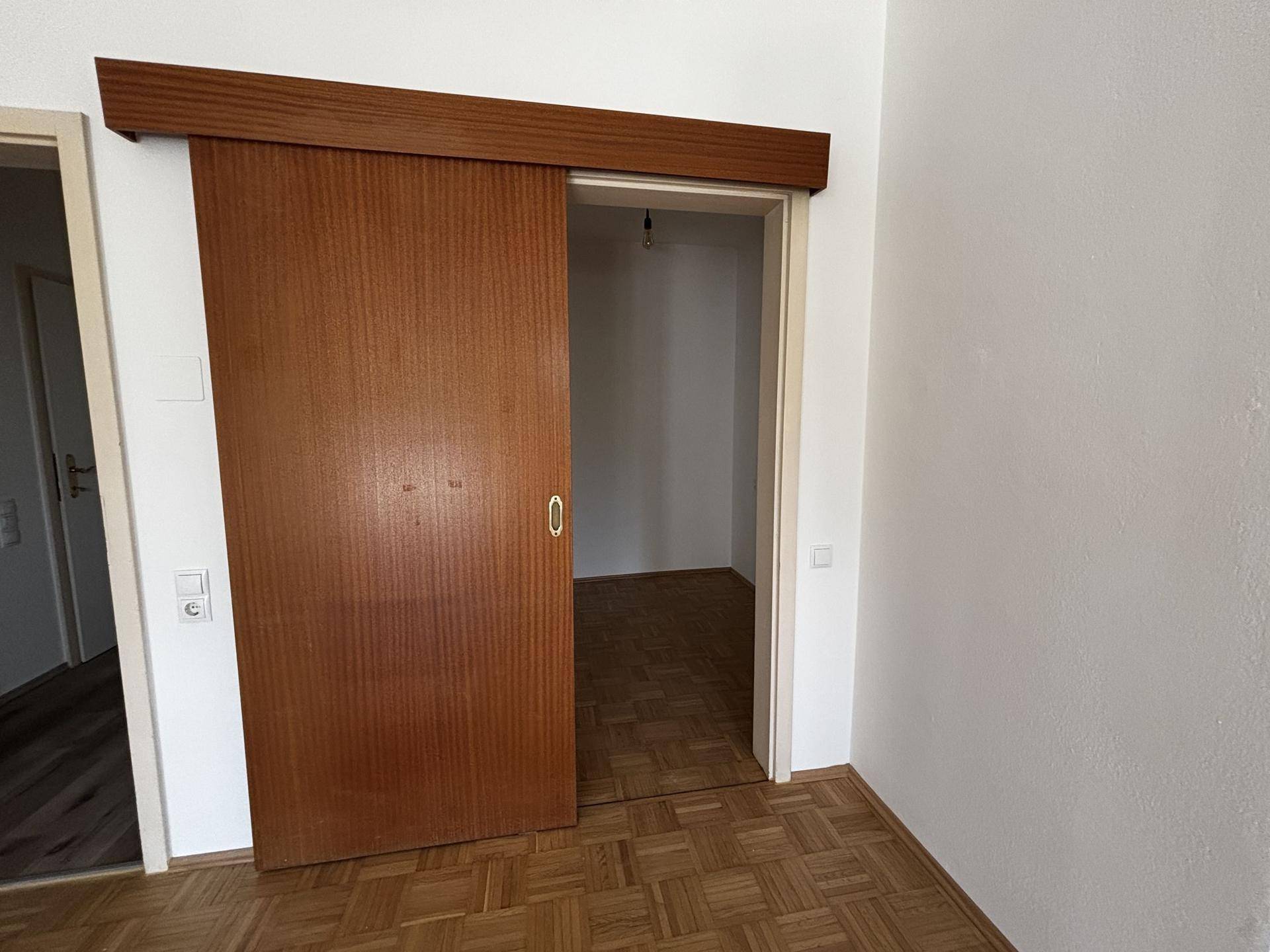Innenraum mit Holzboden und einer braunen Schiebetür, die zu einem weiteren Zimmer führt.