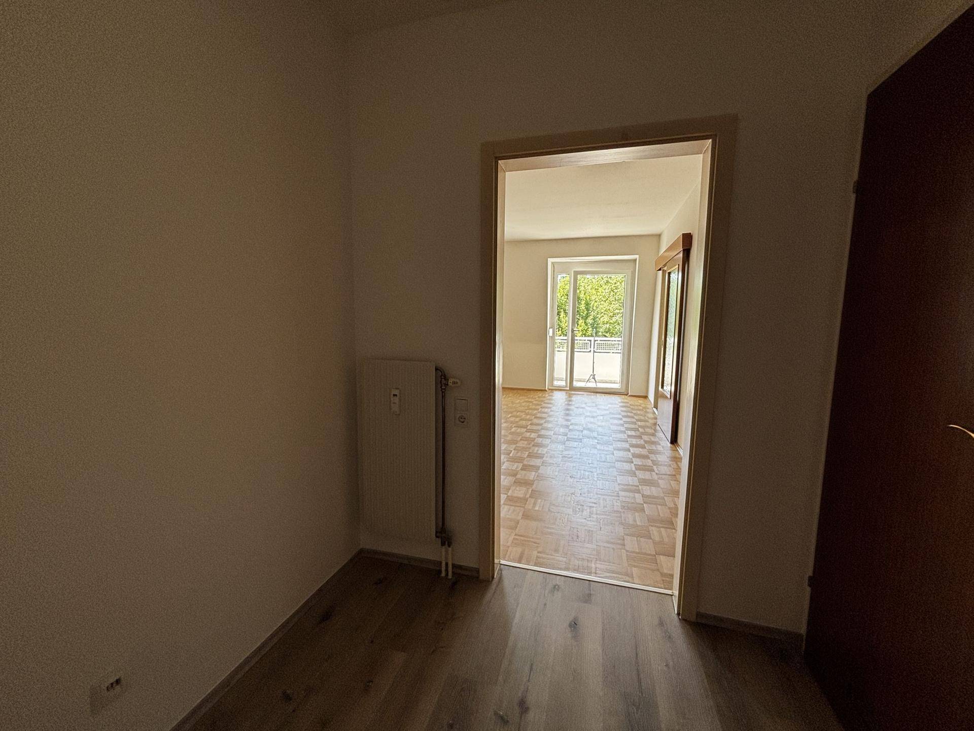 Flur mit Holzboden und Blick in einen angrenzenden Raum mit Parkett und Tageslicht.