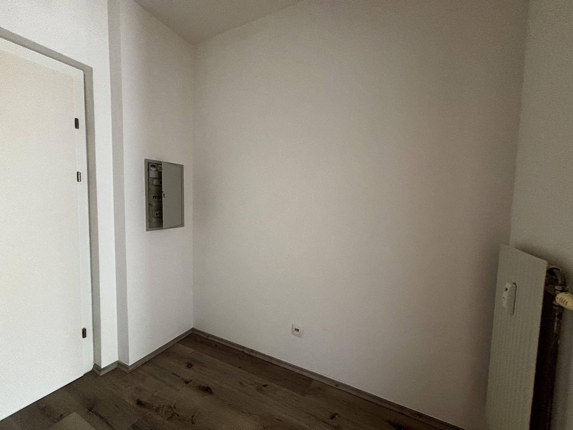 Leerer Raum mit Holzboden und einem Sicherungskasten an der Wand, ideal als Abstellraum.