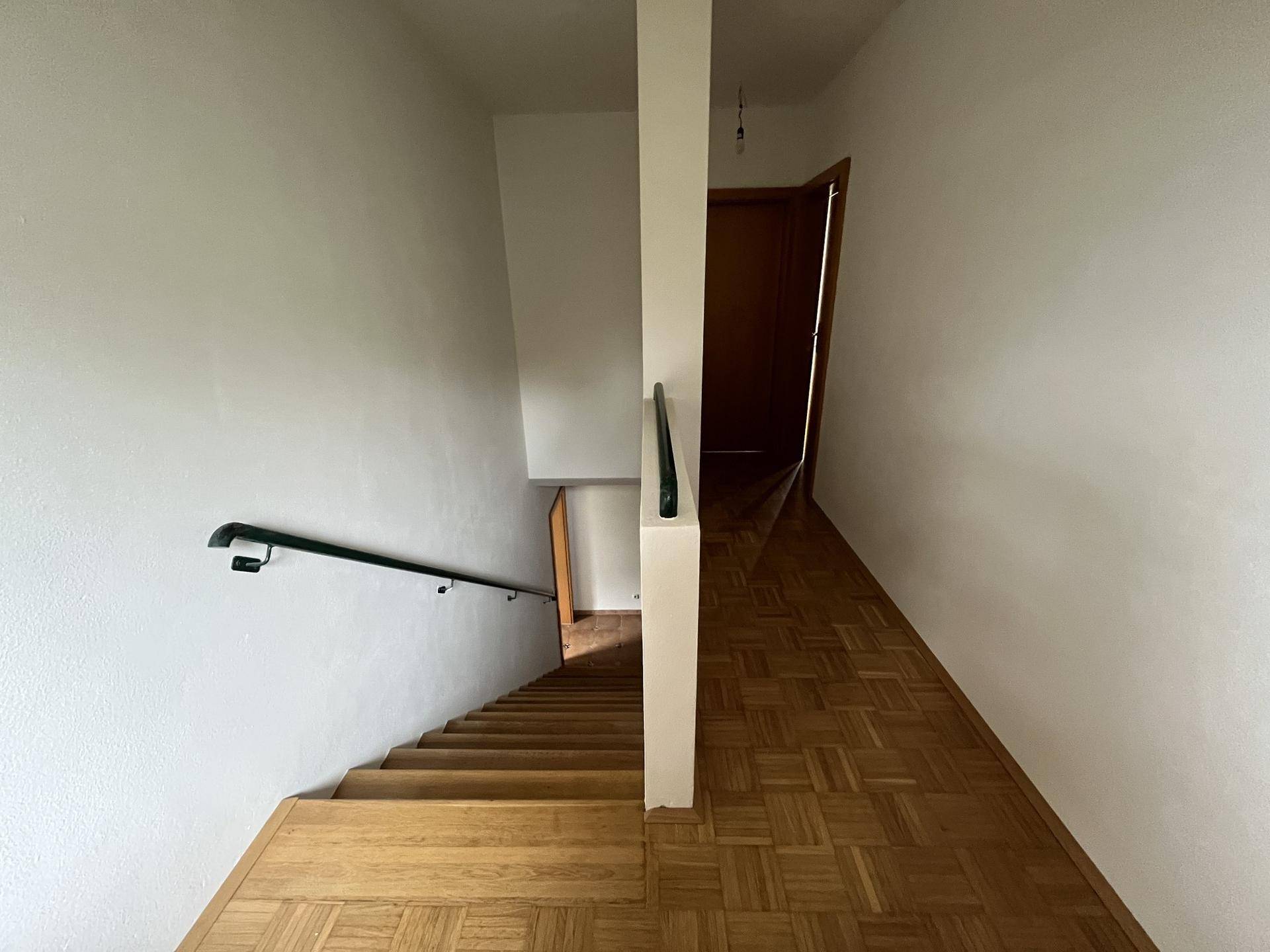 Blick vom oberen Treppenabsatz auf den Flur mit Parkettboden und Treppe nach unten.