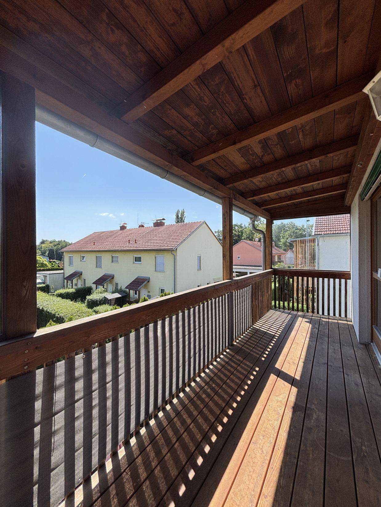 Großer überdachter Holzbalkon mit Geländer und weitem Blick auf die Nachbarschaft.